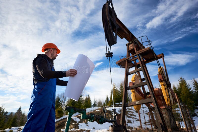 Oljearbetare som står i oljefältet bredvid ett pumputtag med stort papper