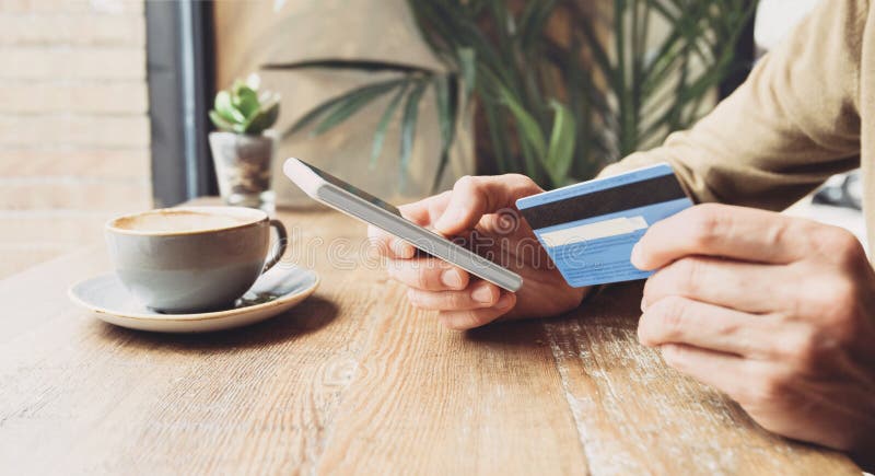 Om care deține cardul de credit și care utilizează telefonul inteligent într-o cafenea care călătorește online pentru comerț elect royalty free stock photo