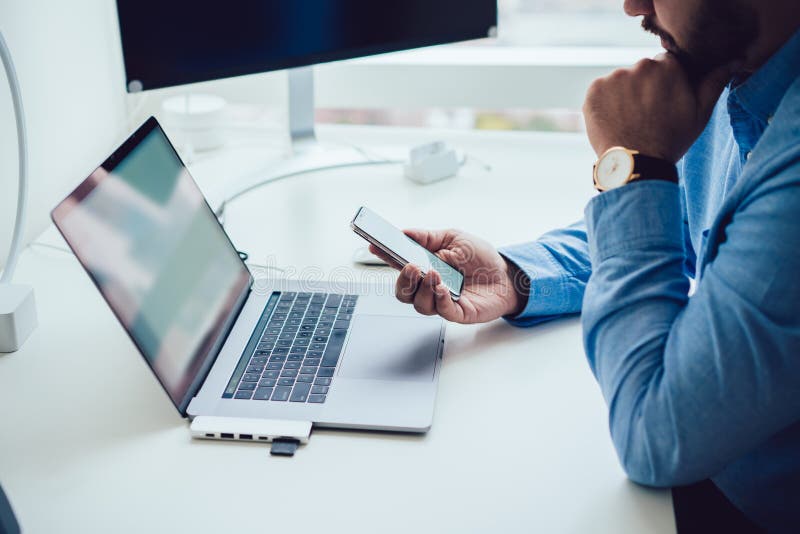 Om care nu poate fi recunoscut, care utilizează smartphone în timp ce lucrează pe laptop stock image