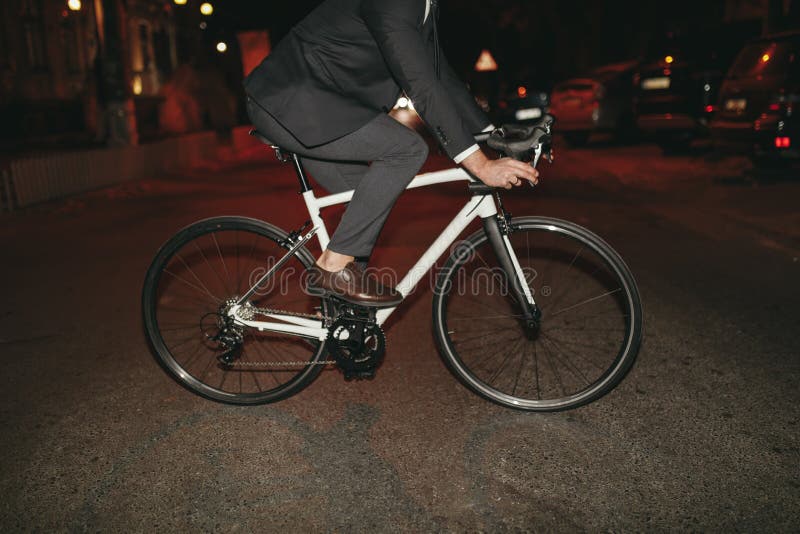 Om de afaceri bine îmbrăcat care merge cu bicicleta în oraș seara royalty free stock photo