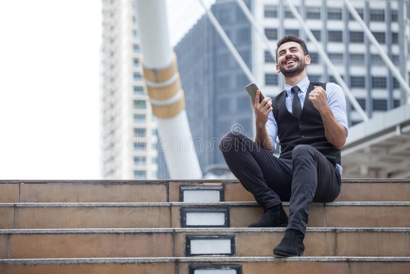 Om de afaceri vesel sărbătorește succesul cu telefonul mobil stând pe scări în oraș în aer liber, căutând vești bune royalty free stock images