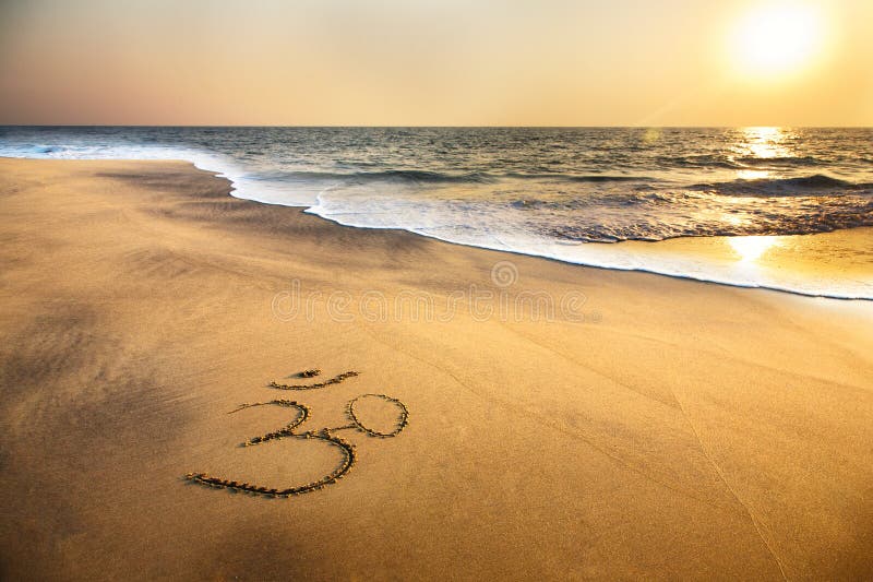 Simbolo Om sulla sabbia della spiaggia, vicino al mare.