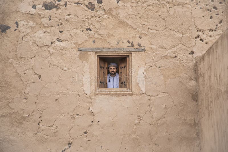 Arab man in traditional omani outfit looking out of a window