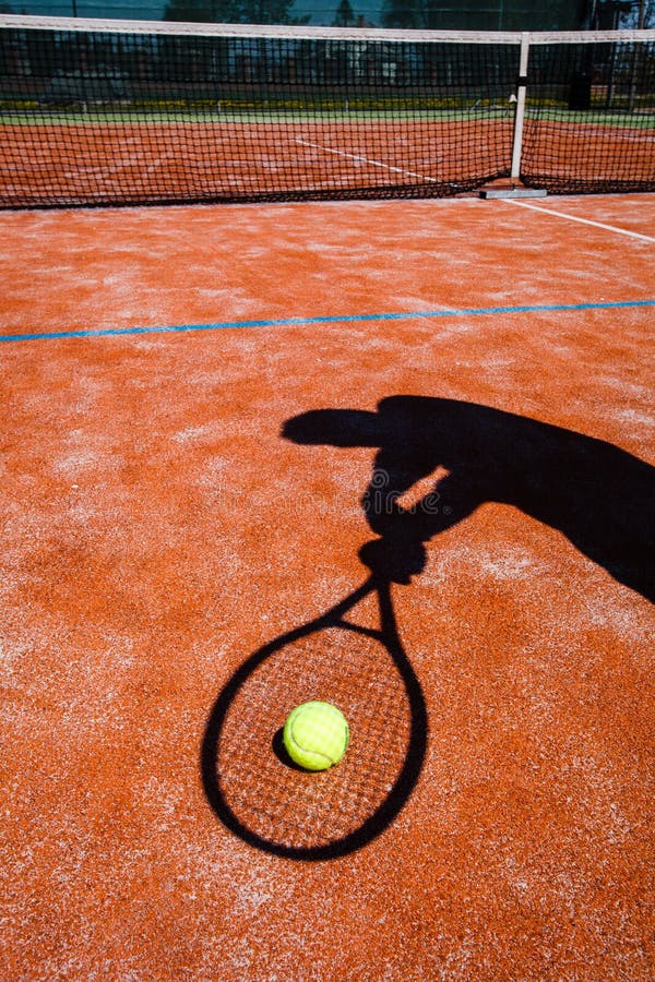 Shadow of a tennis player in action on a tennis court (conceptual image with a tennis ball lying on the court and the shadow of the player positioned in a way he seems to be playing it). Shadow of a tennis player in action on a tennis court (conceptual image with a tennis ball lying on the court and the shadow of the player positioned in a way he seems to be playing it)