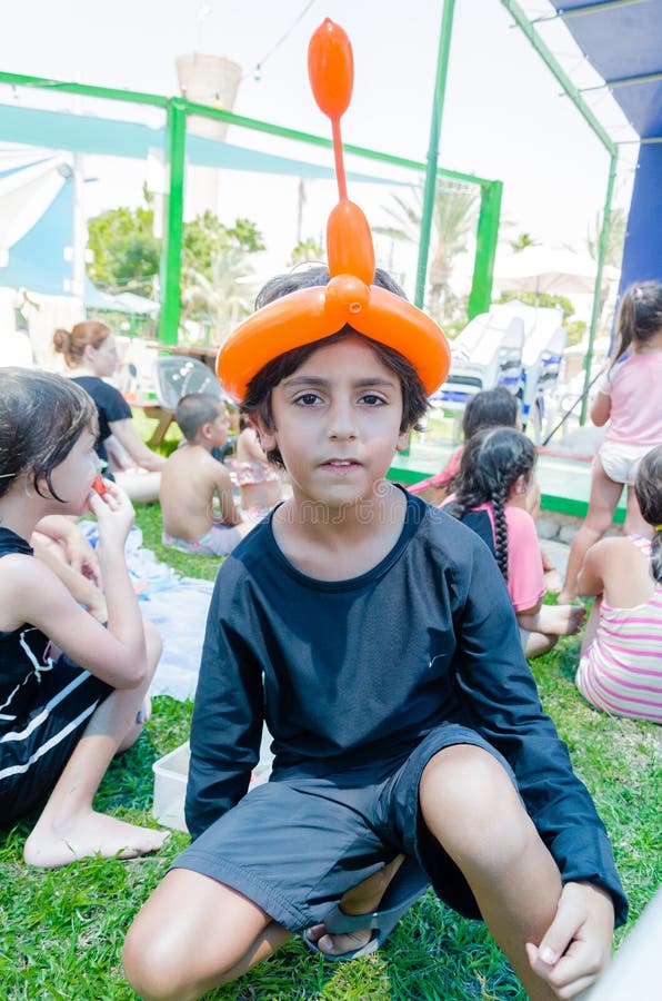 Omer, ISRAELE - adolescente che si siede sull'erba con altri bambini con la palla gonfiabile sulla sua testa sotto forma di turba immagine stock libera da diritti Omer, ISRAELE - adolescente che si siede sull'erba con altri bambini con la palla gonfiabile sulla sua testa sotto forma di turba immagine stock libera da diritti