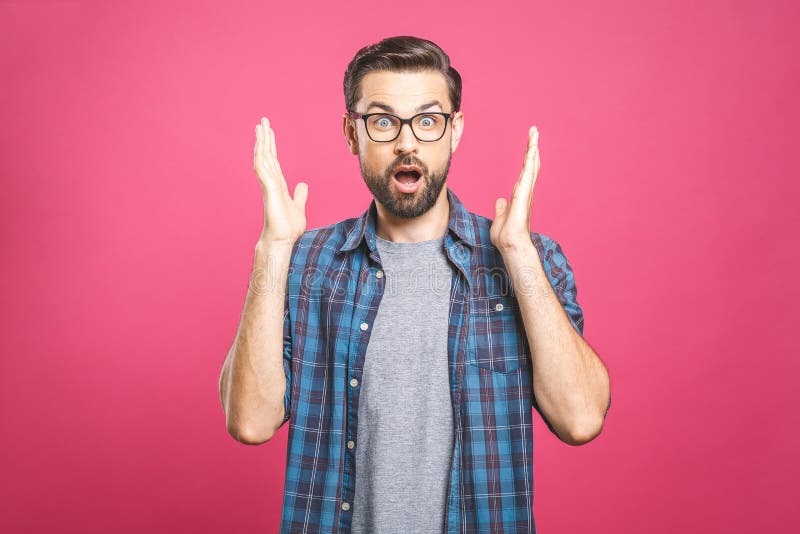 OMG! It`s incredible! Portrait of handsome young man in glasses looking at camera while standing against pink background. Close u