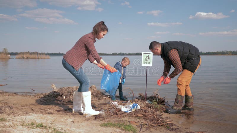 Omsorgnaturekologi, familjvolontärer med den lilla sonen som gör ren upp plast- och polyetylenavfall på smutsig strand