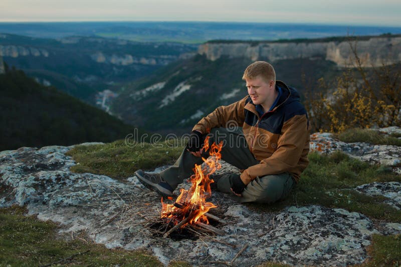 Omul stă lângă un foc care arde în munți stock photo
