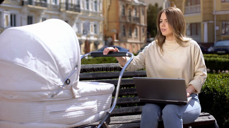 Onbevreesde vrouwelijke freelancer die probeert de huilende baby in de wandelaar te kalmeren royalty-vrije stock foto Onbevreesde vrouwelijke freelancer die probeert de huilende baby in de wandelaar te kalmeren royalty-vrije stock foto
