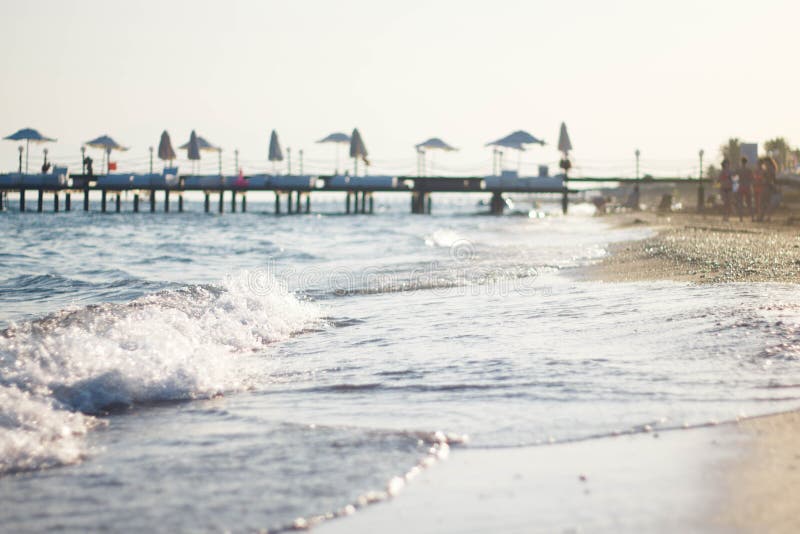 Onda blanca en la playa arenosa La orilla del mar azul contra el embarcadero Embarcadero por el mar en Turquía imágenes de archivo libres de regalías Onda blanca en la playa arenosa La orilla del mar azul contra el embarcadero Embarcadero por el mar en Turquía imágenes de archivo libres de regalías