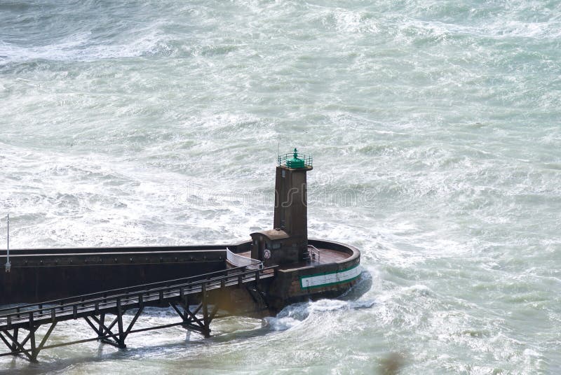 Ondas altas da vista que deixam de funcionar um farol perto da costa com o mar azul do aqua do fundo e a ponte de madeira escura, imagem de stock Ondas altas da vista que deixam de funcionar um farol perto da costa com o mar azul do aqua do fundo e a ponte de madeira escura, imagem de stock