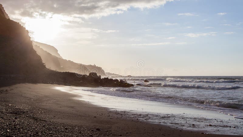 Ondas que quebram na costa de uma praia de Tenerife com luz traseira do por do sol próximo imagem de stock Ondas que quebram na costa de uma praia de Tenerife com luz traseira do por do sol próximo imagem de stock