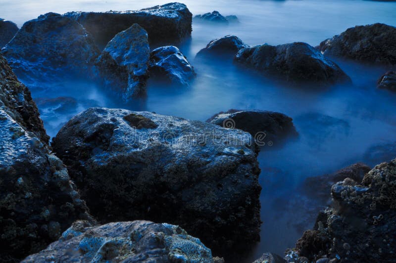 Closeup of sea waves breaking on coastal rocks at dusk with blue color tone. Closeup of sea waves breaking on coastal rocks at dusk with blue color tone.