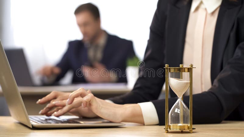 Onderneemster die aan computer, zandloper werken die, resultatenanticiperen druppelen royalty-vrije stock foto Onderneemster die aan computer, zandloper werken die, resultatenanticiperen druppelen royalty-vrije stock foto