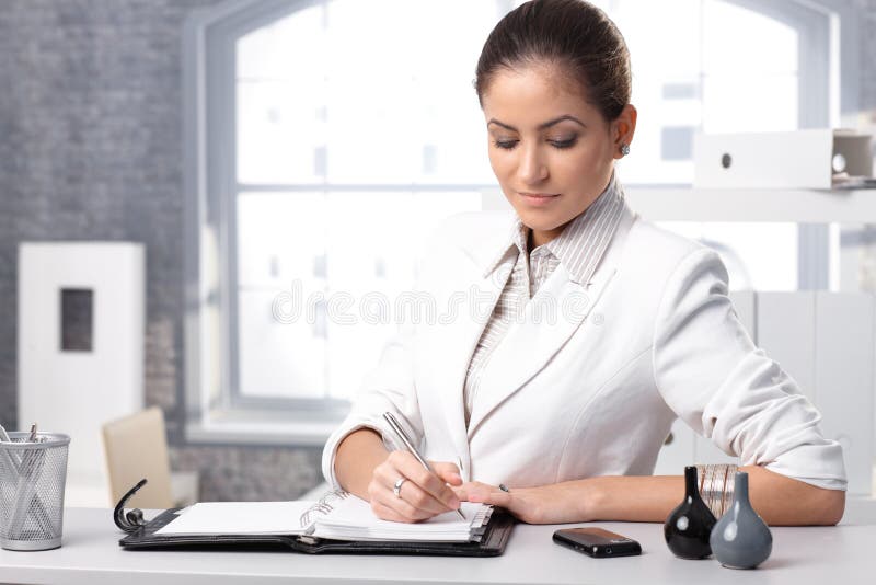 Businesswoman concentrating, taking notes at office desk. Businesswoman concentrating, taking notes at office desk.