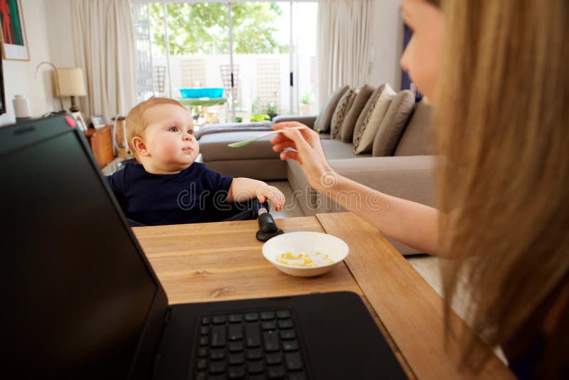 Onderneemster thuis en voedende baby die werken royalty-vrije stock afbeeldingen Onderneemster thuis en voedende baby die werken royalty-vrije stock afbeeldingen