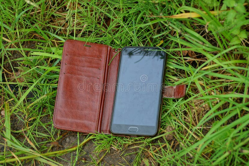 One black smartphone in an open brown leather case lies on the green grass