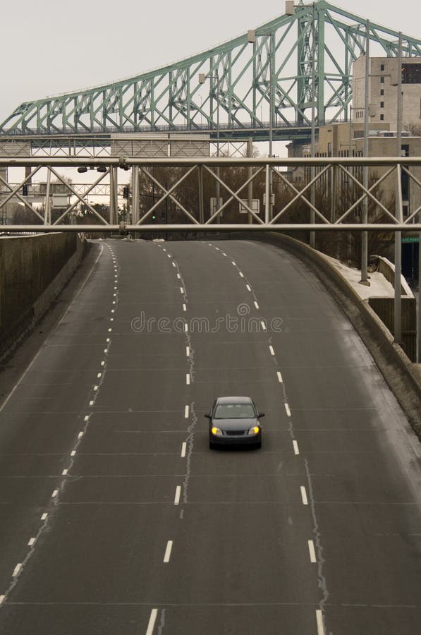 One car on four lane highway on the road in an american town driving on the tarmac with bridge in background. One car on four lane highway on the road in an american town driving on the tarmac with bridge in background