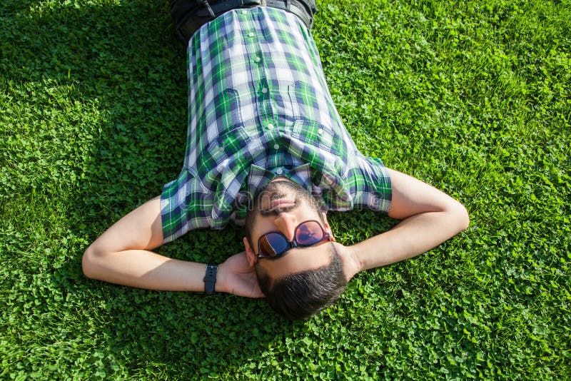 One fashion middle eastern man with beard, fashion hair style is resting on beautiful green grass day time.