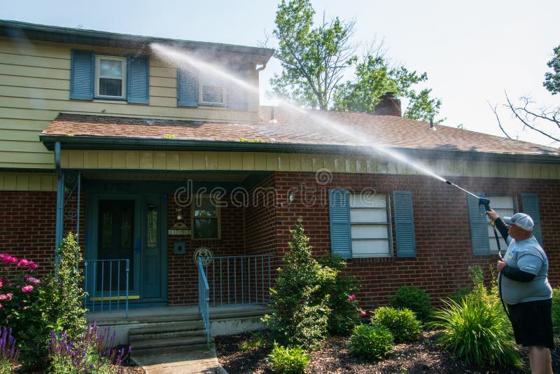 One heavy overweight Caucasian man spraying water solution on the front of a house as part of his pressure washing service. The royalty free stock photo One heavy overweight Caucasian man spraying water solution on the front of a house as part of his pressure washing service. The royalty free stock photo