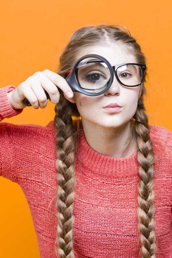 One Intelligent Caucasian Girl in Glasses And Coral Knitted Sweater Holding Big Magnifying Glass While Searching And Looking