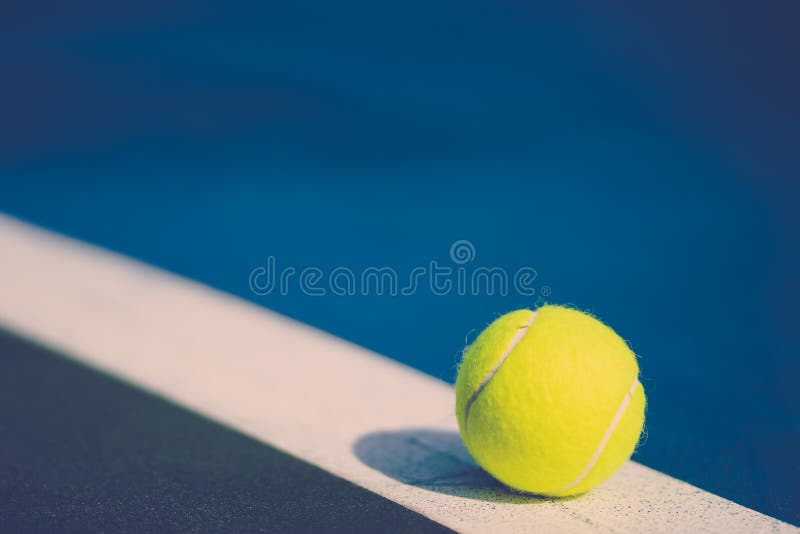 One new tennis ball on white diagonal line in blue hard court with light from right, vintage tone