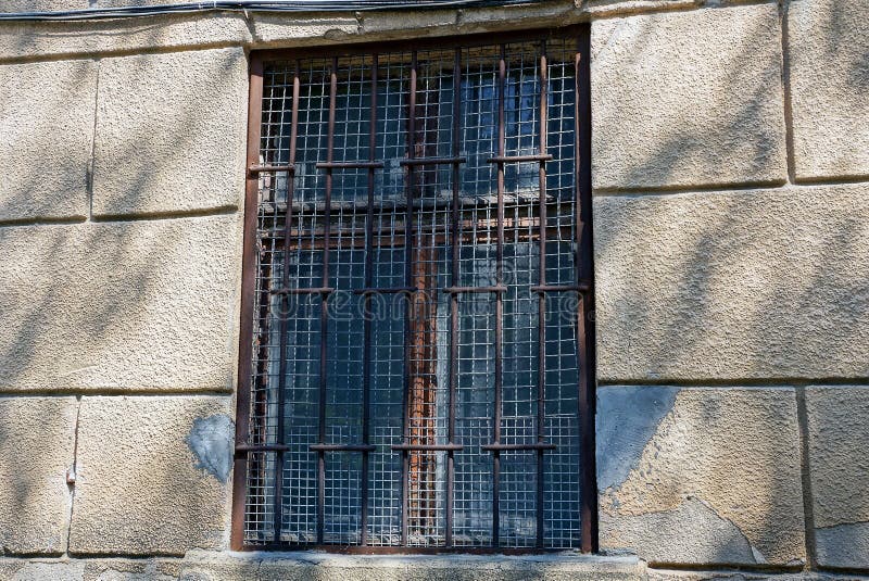 Old brown window behind bars on a gray concrete wall