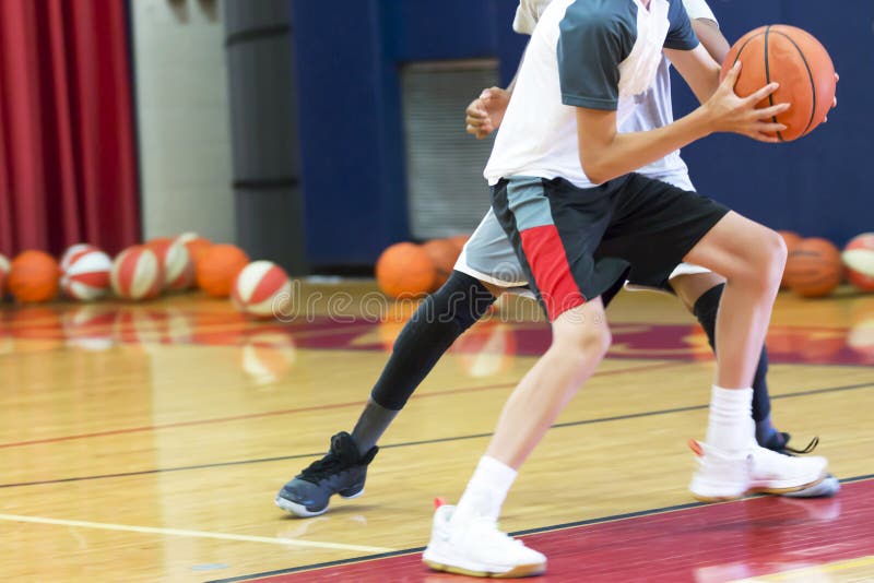 Two teenage male basketball players doing a one on one drill indoors at a local basketball camp over the summer. Two teenage male basketball players doing a one on one drill indoors at a local basketball camp over the summer.