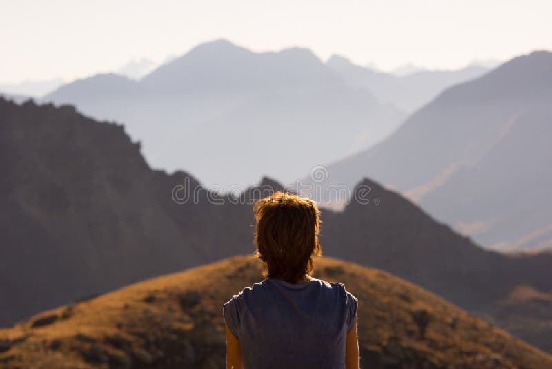 One person looking at view high up on the Alps. Expasive landscape, idyllic view at sunset. Rear view.