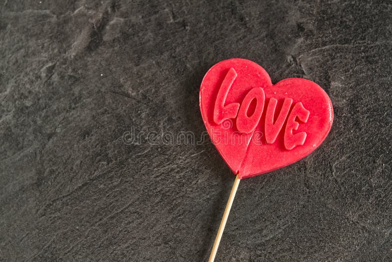 One red candy lollipop heart shape with `love` inscription. One candy lollipop heart shape with `love` inscription on dark background stock image One red candy lollipop heart shape with `love` inscription. One candy lollipop heart shape with `love` inscription on dark background stock image
