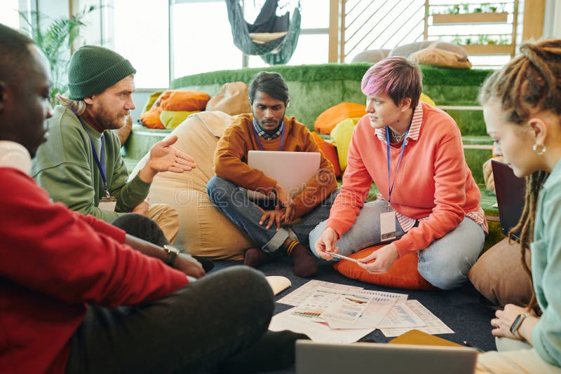 Group of young intercultural financial managers in casualwear discussing papers. One of several young intercultural financial managers pointing at diagram on paper while explaining data to colleagues at working meeting