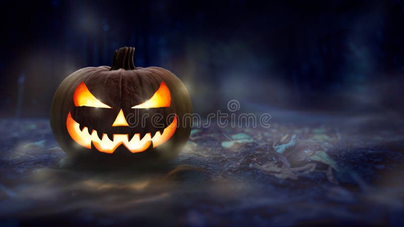 One spooky halloween pumpkin, Jack O Lantern, with evil face and glowing eyes on a leaf covered forest floor at night. One spooky halloween pumpkin, Jack O Lantern, with evil face and glowing eyes on a leaf covered forest floor at night