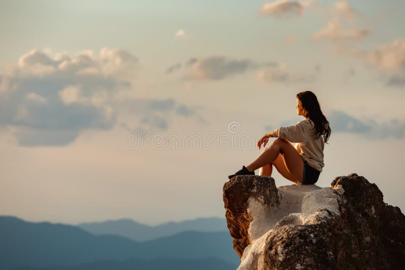 Sporty girl sits on big rock against sunset and mountains