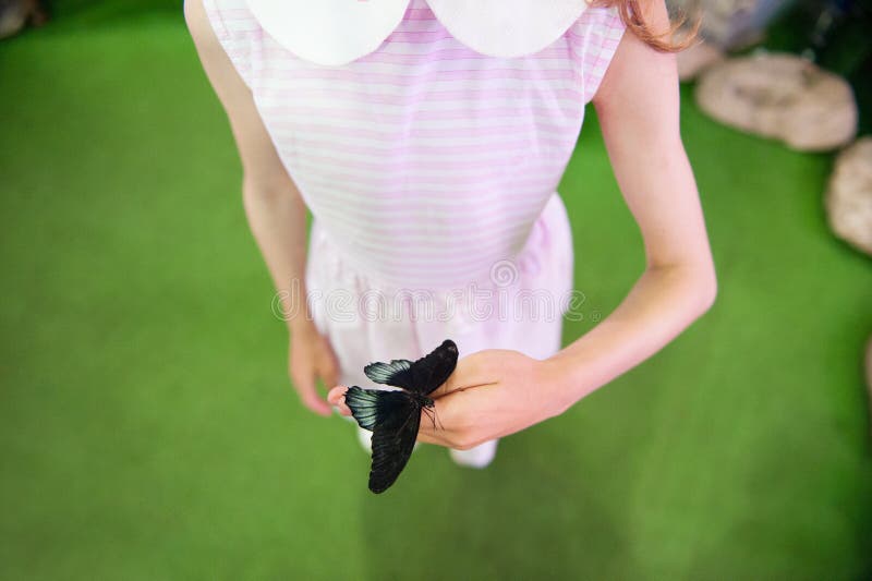 One thin little girl in summer dress holding black butterfly insect on her hand in insectarium education learning tour