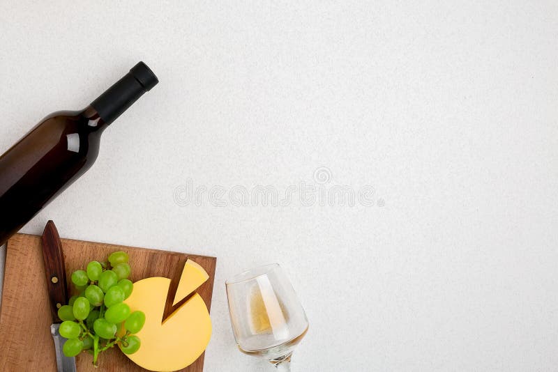 One wine glass with white wine, bottle of white wine, cheese on white background. Horizontal view from the top.