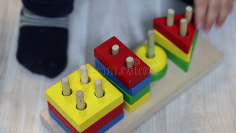 A one year old child puts geometric shapes on pin in wooden construction. Close-up of kid's hand and toy stock video