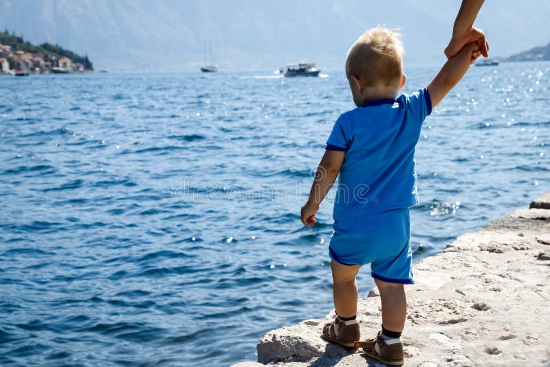 One year old child stands on the edge of the pier and looks at the Bay of Kotor in Montenegro, view from the back royalty free stock photo One year old child stands on the edge of the pier and looks at the Bay of Kotor in Montenegro, view from the back royalty free stock photo