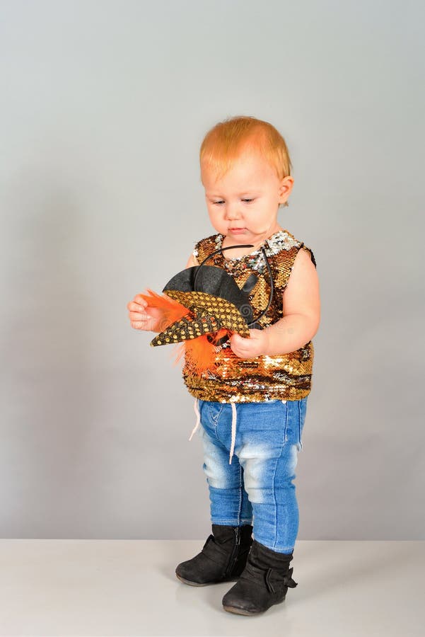 A one-year-old girl holds a hat in her hands and looks at her. A small child in jeans and sequins poses in a modeling agency. royalty free stock photo A one-year-old girl holds a hat in her hands and looks at her. A small child in jeans and sequins poses in a modeling agency. royalty free stock photo