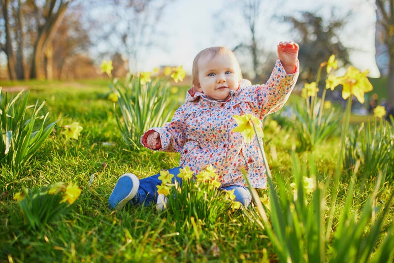 One year old girl sitting on the grass with yellow narcissi