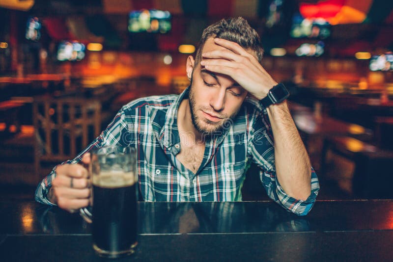 One Young Man Sit Alone at Bar Counter in Pub. he Hold Mug of Dark Beer ...