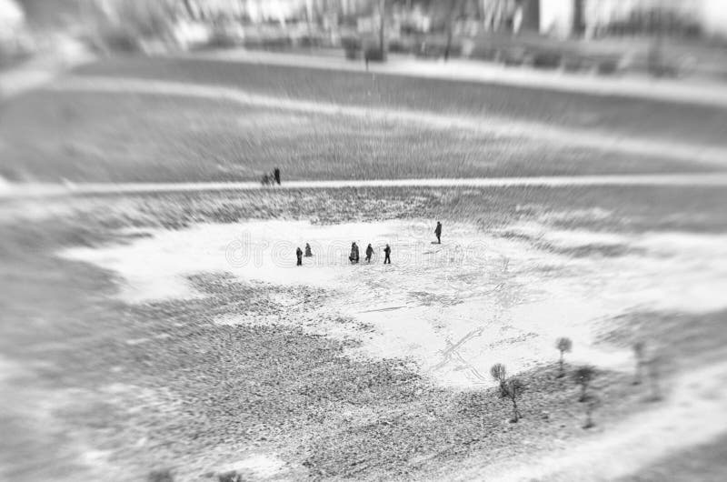 Unusual view from afar of unidentified adults and children walking in a large puddle covered with ice and snow in the city square in the black and white style. Unusual view from afar of unidentified adults and children walking in a large puddle covered with ice and snow in the city square in the black and white style