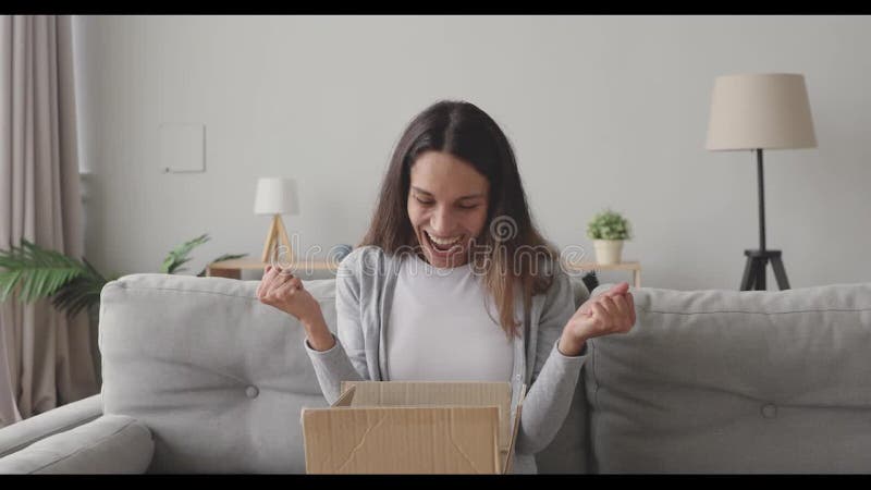 Ongelofelijke jonge vrouw die een kartonnen doos opent met internetwinkelbestelling