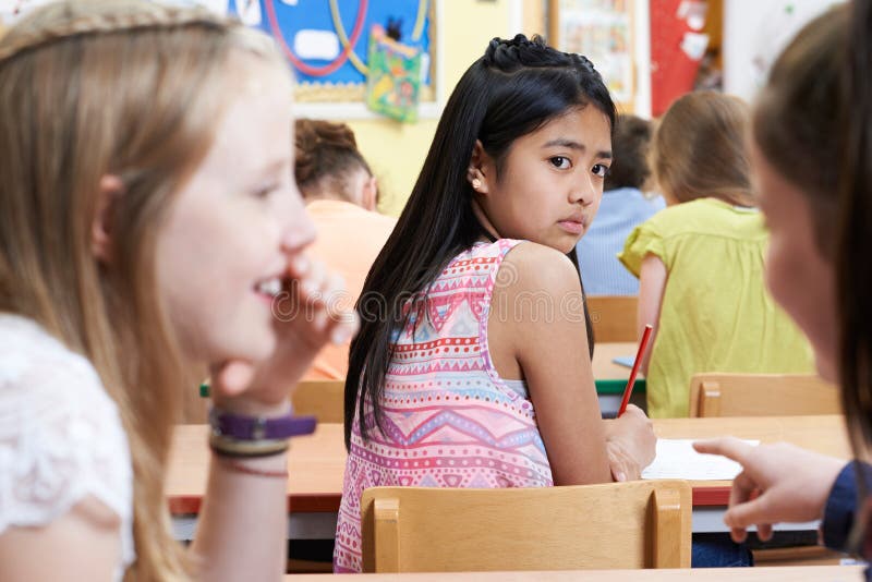 Ongelukkig Meisje die ongeveer door Schoolvrienden worden geroddeld in Klaslokaal royalty-vrije stock fotografie Ongelukkig Meisje die ongeveer door Schoolvrienden worden geroddeld in Klaslokaal royalty-vrije stock fotografie