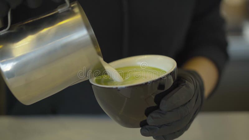 Onherkenbare barman die melk toevoegt aan matcha green tea. het sluiten van de handen in beschermende zwarte handschoenen die gezo