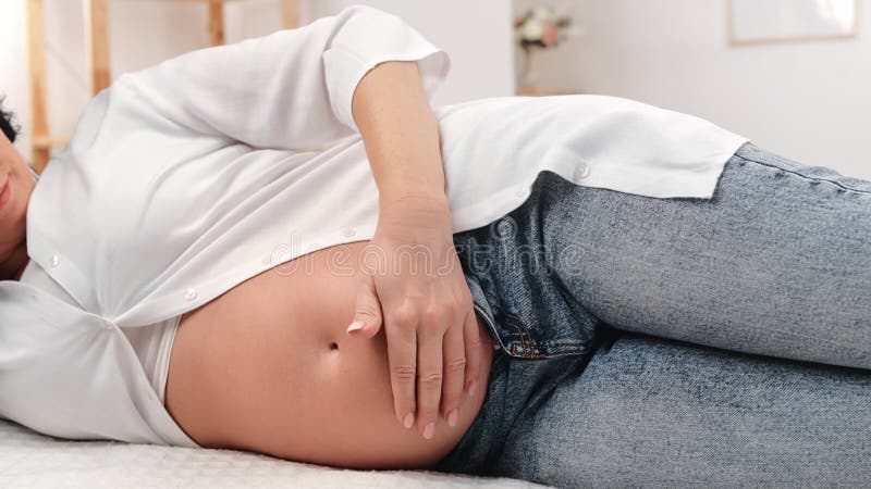 Onherkenbare zwangere vrouw die de tumor aanraakt geniet van moederschapszorg die tapijtvloer bij thuiszorg ligt .