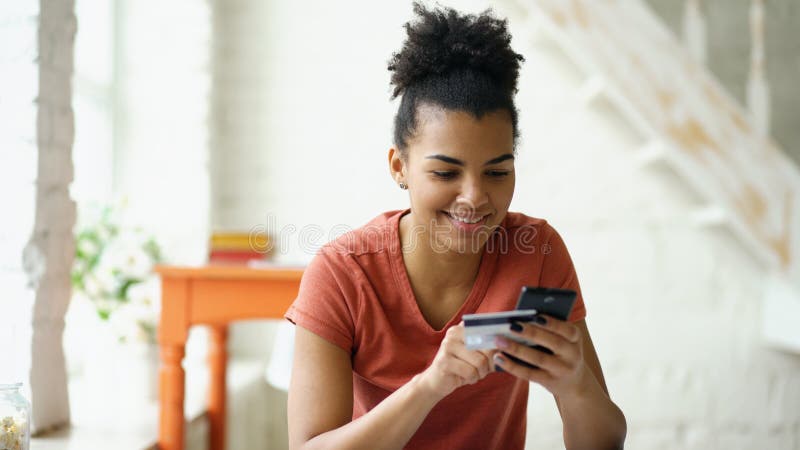 Online-bankrörelsen för härlig lycklig kvinna för blandat lopp genom att använda smartphonen som direktanslutet shoppar med hemma