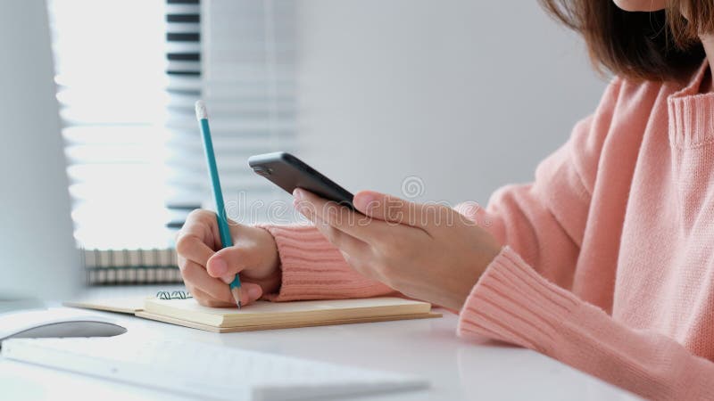 Online study, Woman hand writing on notebook while using mobile phone for digital home study class, Adult female student doing royalty free stock photo