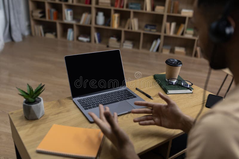 Online video call and communication. Over the shoulder view of man sitting at table using laptop with black empty screen stock photography