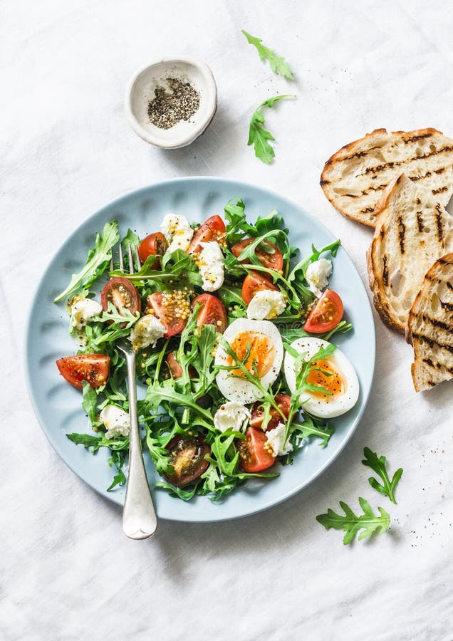 Ontbijtsalade - arugula, kersentomaten, mozarella en gekookt ei met olijfolie, mosterd die, citroen zich op licht kleden backgrou royalty-vrije stock foto's Ontbijtsalade - arugula, kersentomaten, mozarella en gekookt ei met olijfolie, mosterd die, citroen zich op licht kleden backgrou royalty-vrije stock foto's