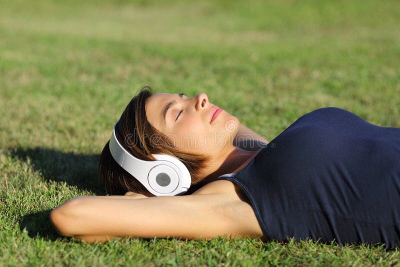 Relaxed woman listening to the music with headphones lying on the grass of a garden. Relaxed woman listening to the music with headphones lying on the grass of a garden